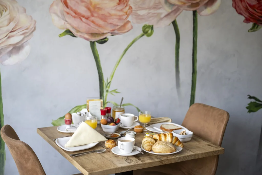 Table du petit-déjeuner dressée devant un mur peint de grandes fleurs