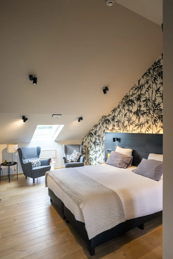 Chambre mansardée avec lit double, fauteuil et papier peint végétal